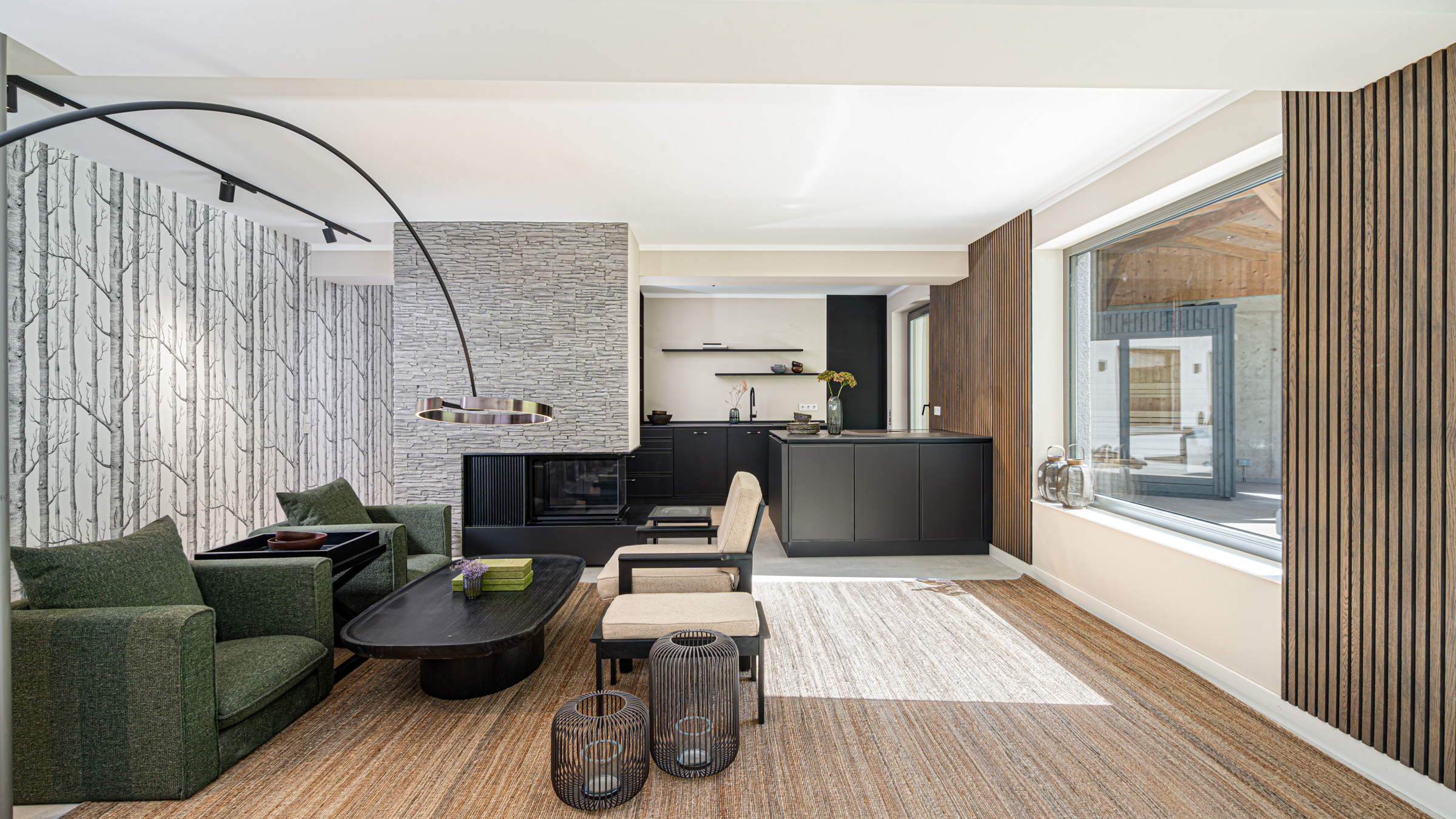 Modern eingerichtetes Chalet-Wohnzimmer mit Kamin, offener Designküche und großen Fenstern – stilvolle Kombination aus Naturstein, Holz und modernen Möbeln