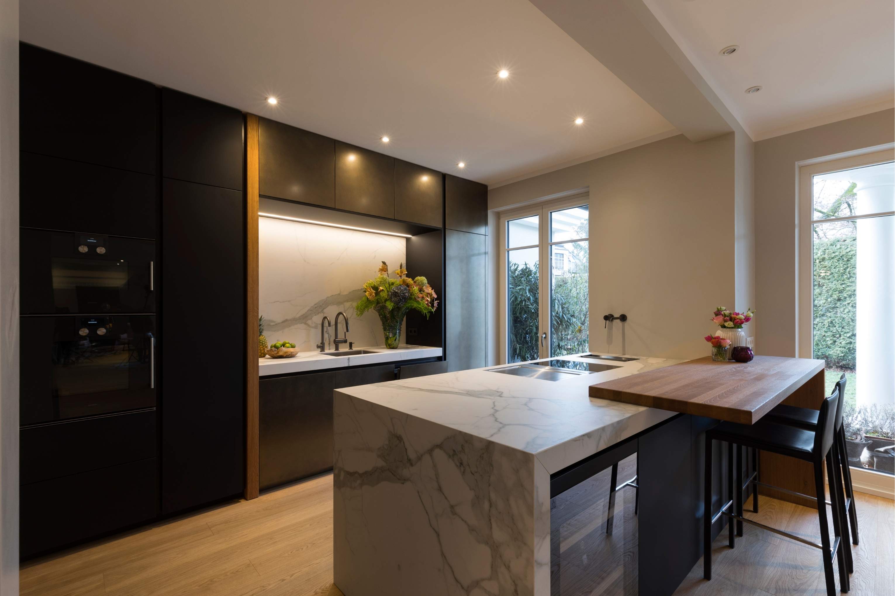 Küche mit dunklen, metallischen Fronten und Insel in Calacatta-Optik