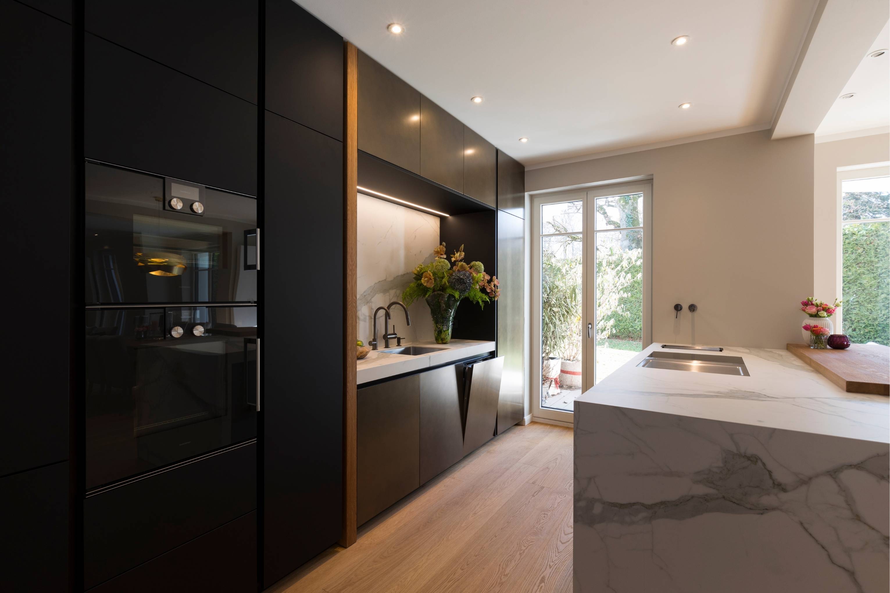 Küche mit dunklen, metallischen Fronten und Insel in Calacatta-Optik