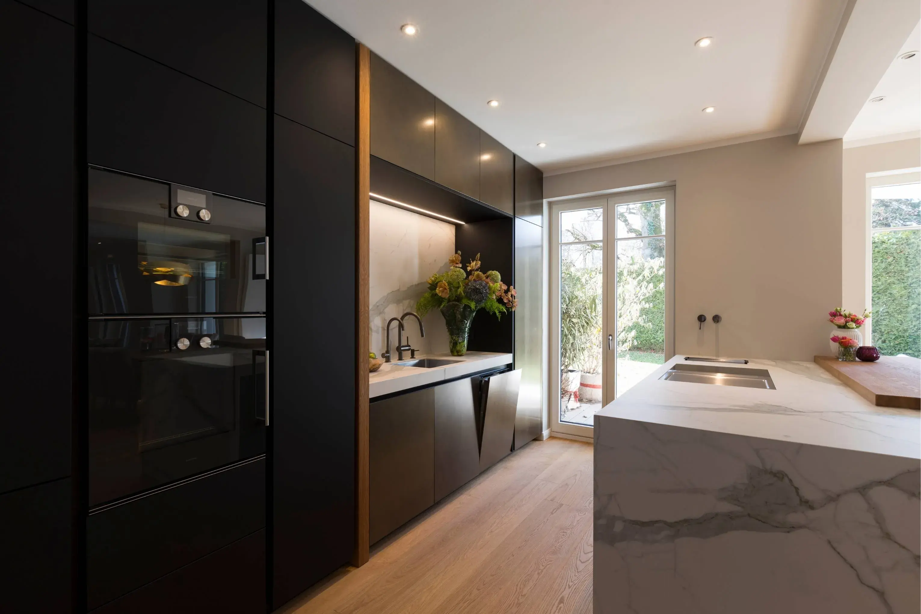 Küche mit dunklen, metallischen Fronten und Insel in Calacatta-Optik